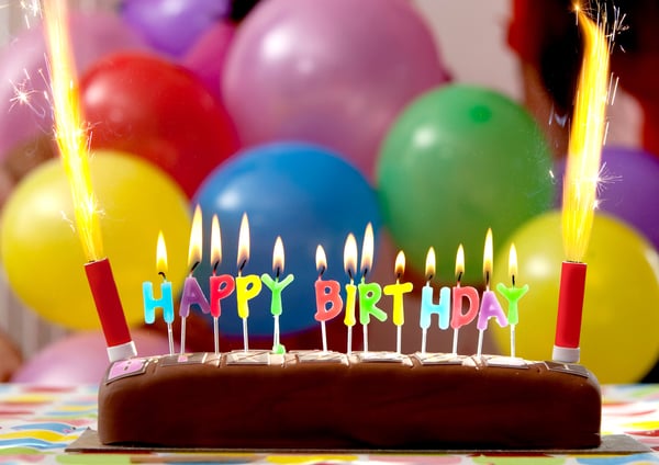 Birthday cake with candles lit up and balloons on the background